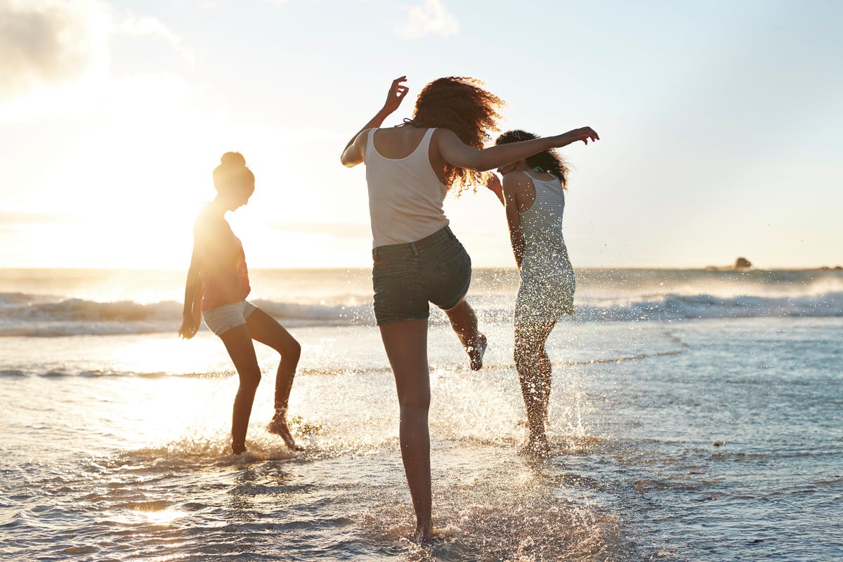 Three young women kicking water and laughing on the beach
