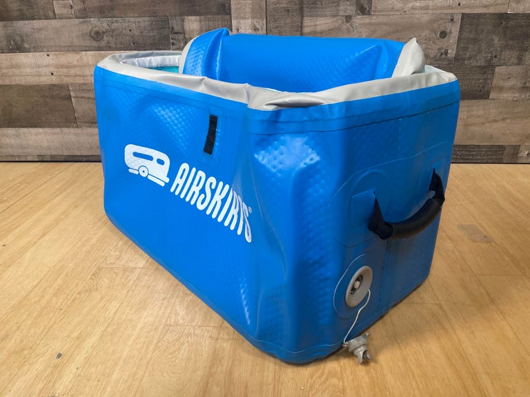The AirSkirts inflatable cooler sits on a wooden floor with its release valve opening, causing it to deflate into something that's easier to store away in a closet or garage.