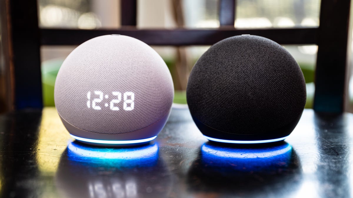 a white Echo Dot with Clock and black Echo Dot on a shiny table