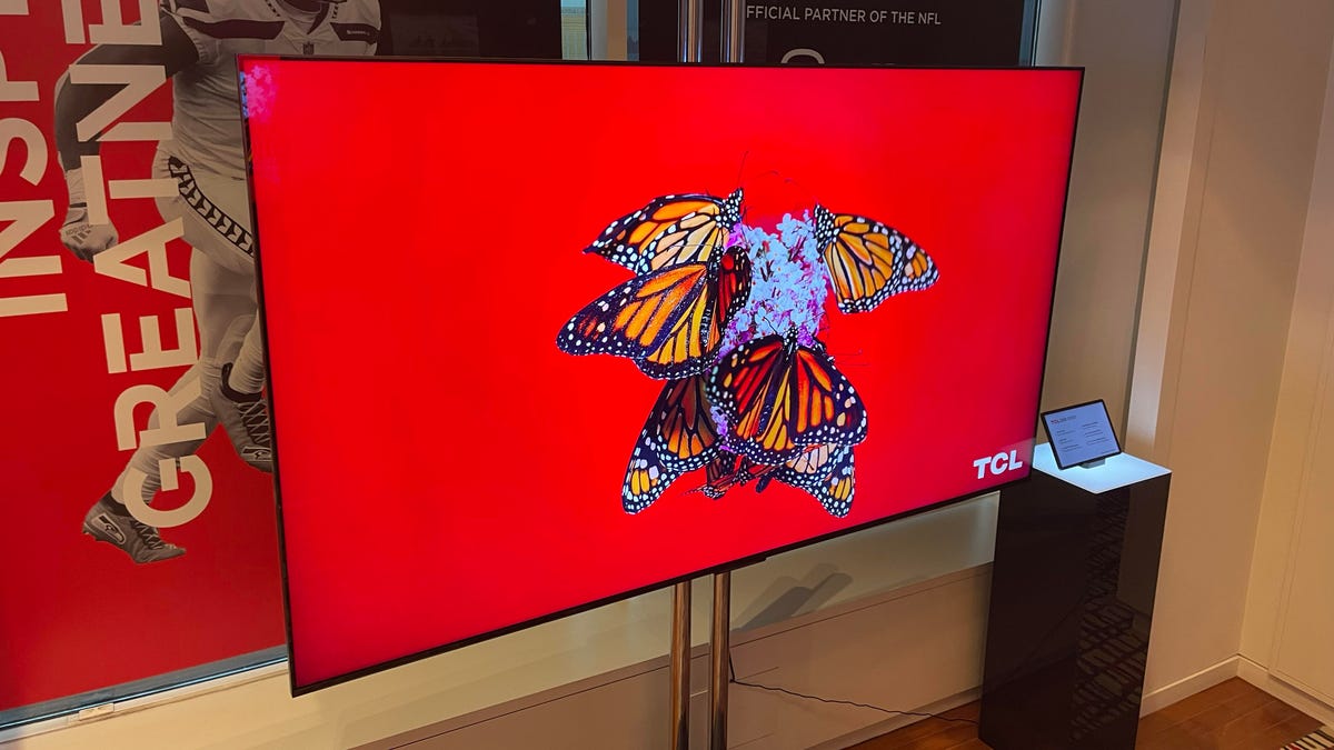 A TCL QM851 TV with a butterfly against a red background.