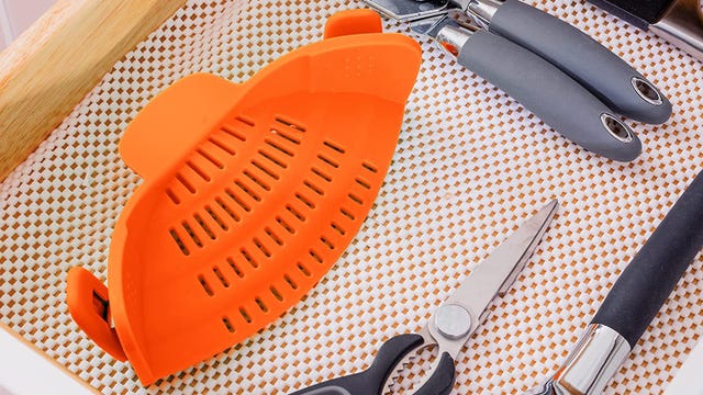 An orange strainer in a drawer of kitchen tools
