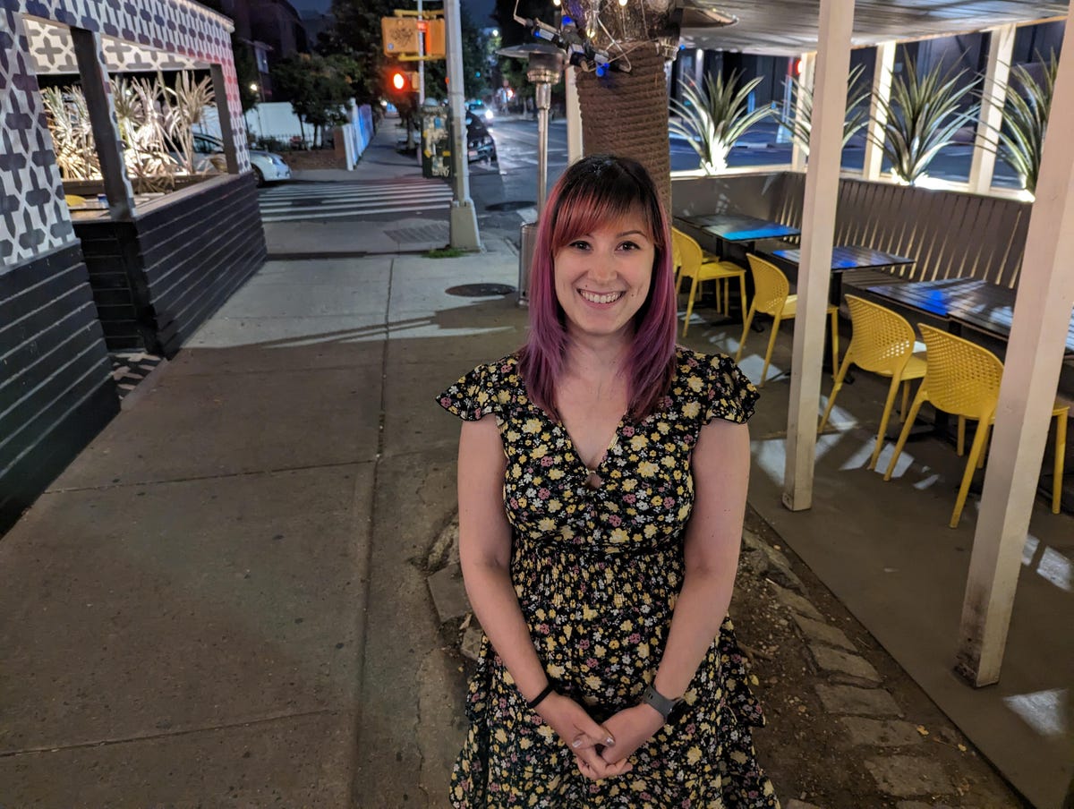 A photo of a woman standing on a sidewalk at night taken with the Pixel 7 Pro.