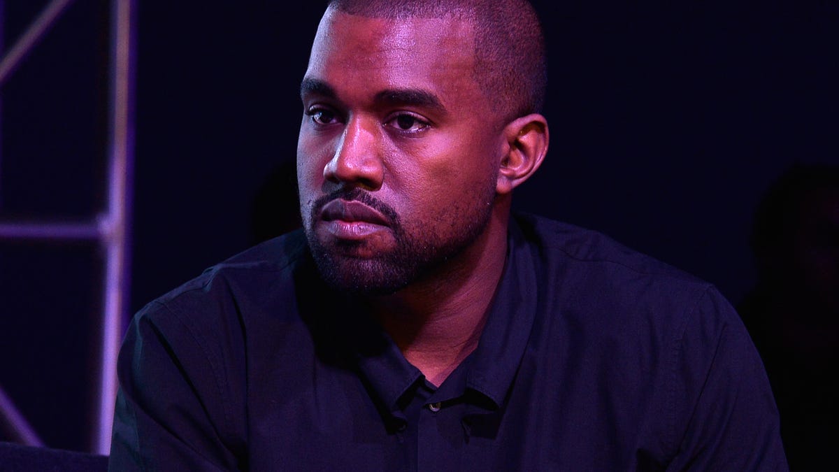 Kanye West sits with a slight violet light cast on his face