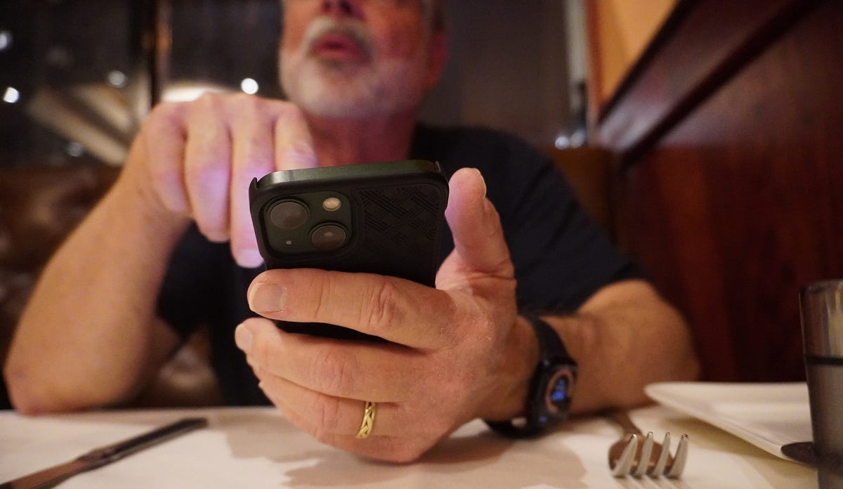 A man holds an iPhone 13 mini and points to various things on screen, asking questions.