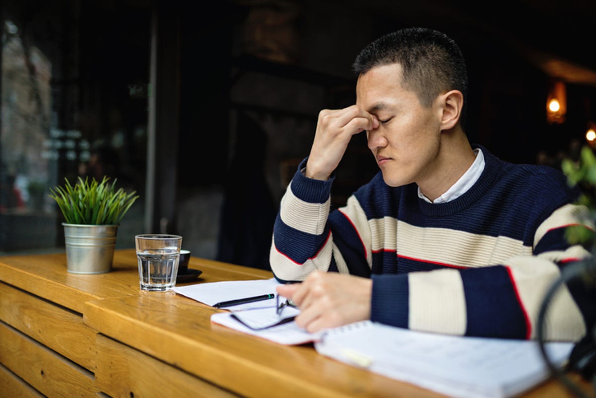 Man sitting in front of an open notebook, pinching nose bridge from stress.