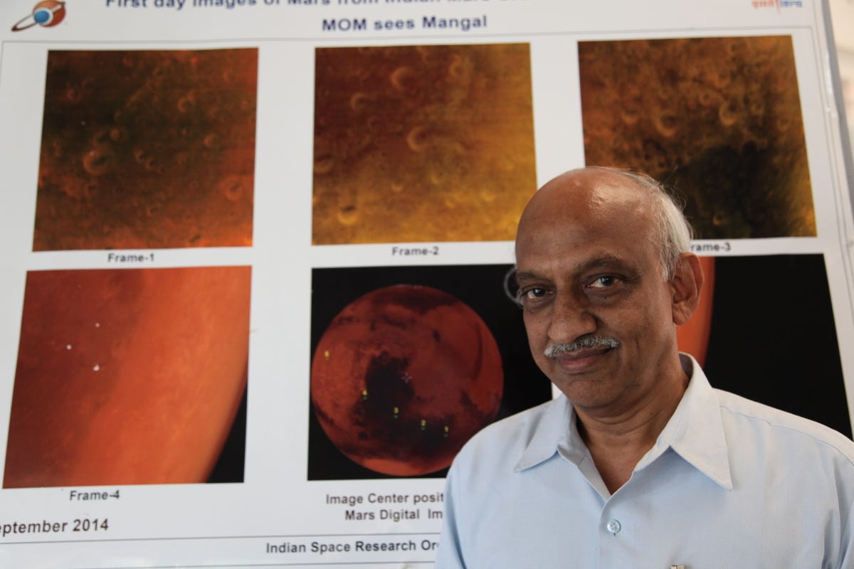 Le Dr Kiran Kumar se tient devant une affiche montrant six vues différentes de Mars.