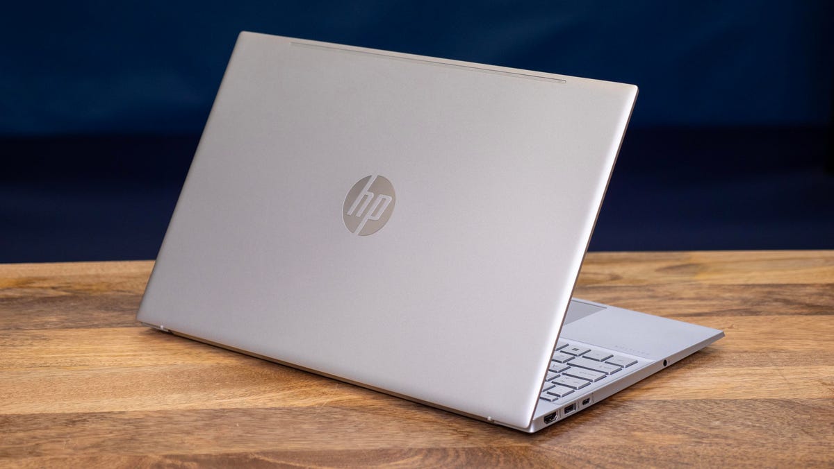 HP Pavilion 15t-eg300 15-inch laptop open rear facing right sitting on a wood desk in front of a dark blue backdrop..