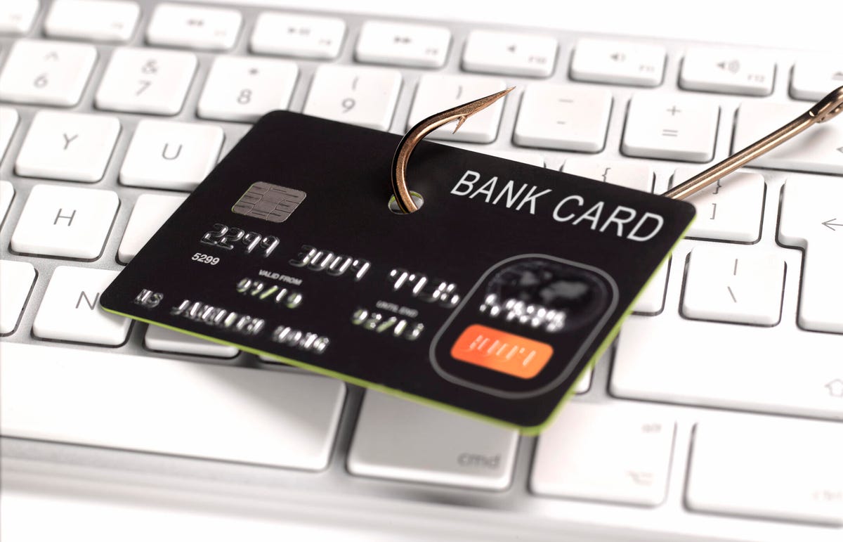 A image of a fish hook hooking a credit card in front of a computer keyboard.