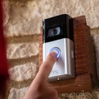A finger presses the button on a mounted Ring Video Doorbell 4.