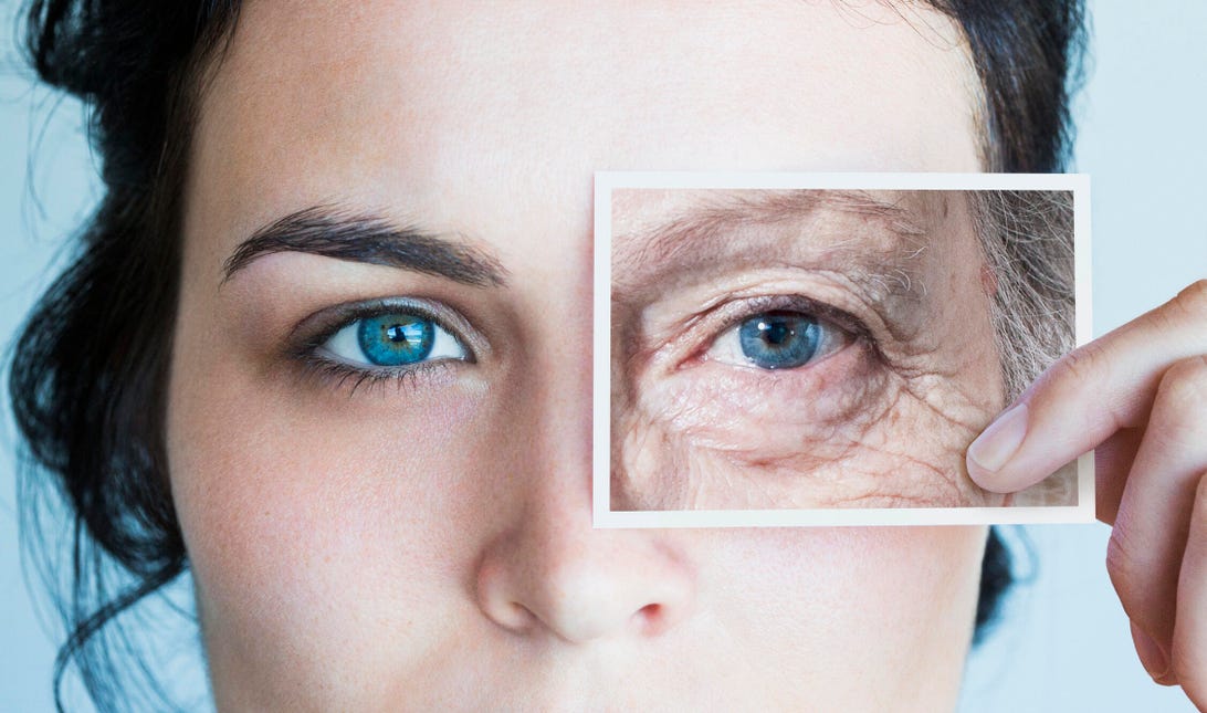 Woman holding photo of older woman's eye in front of her face.