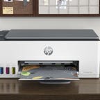 HP Smart Tank printer on a desk with a smartphone next to it