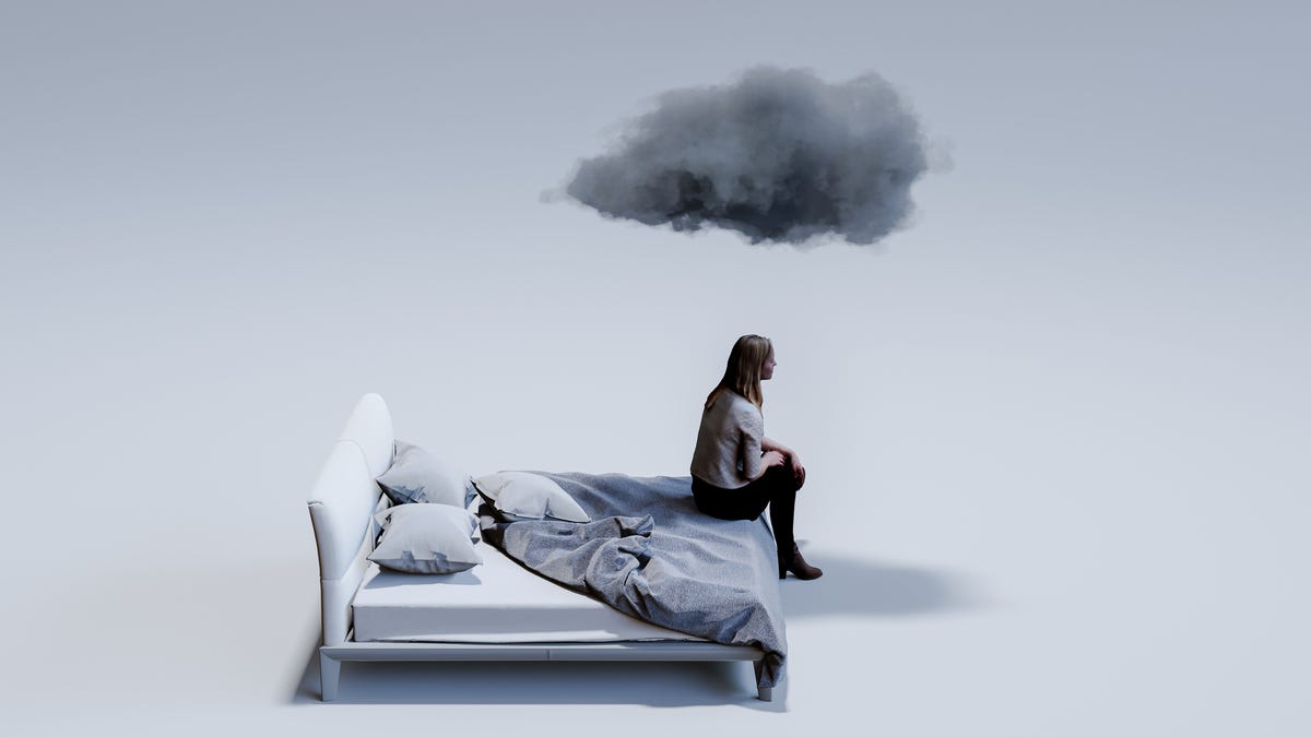 Woman sitting on corner of double bed with dark cloud above head.