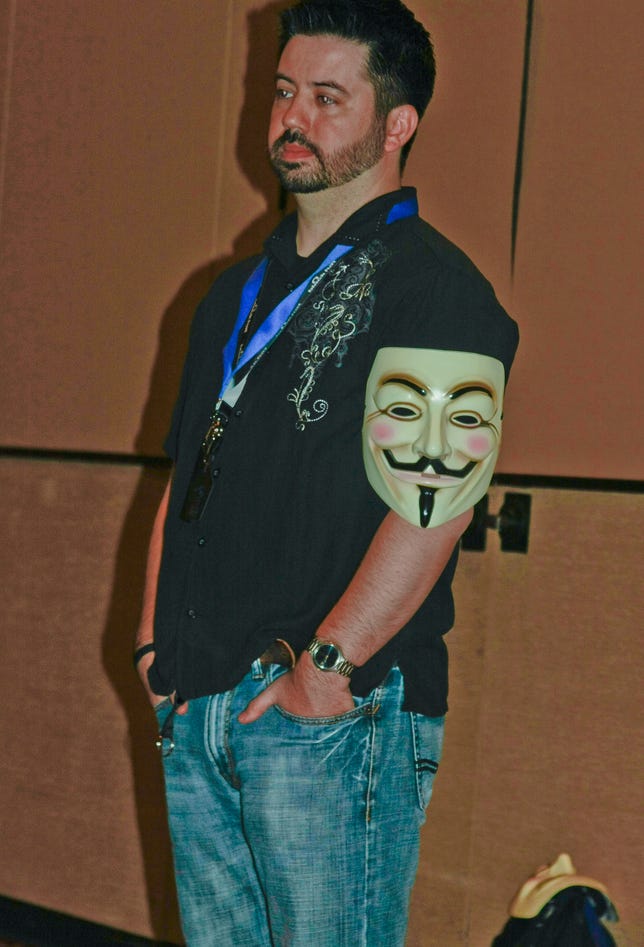 Joshua Corman, director of security intelligence for Akamai, listens to a question from an audience member about the online activist group Anonymous at DefCon 19 in Las Vegas. On his arm is a Guy Fawkes mask as depicted in the comic strip and movie "V for Vendetta," which Anonymous members have appropriated as a logo. Corman is not affiliated with Anonymous.