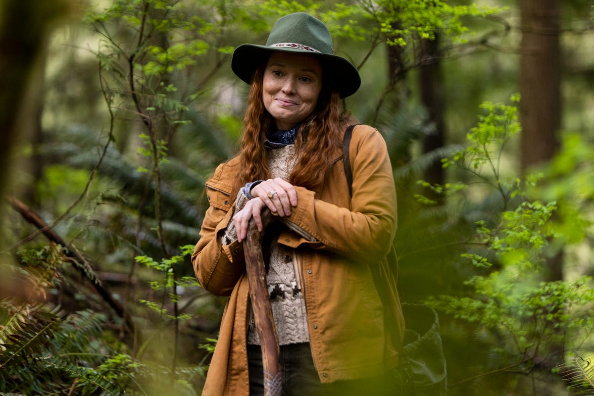 Samantha Sloyan as Shasta, holding a walking stick and smiling in a forest