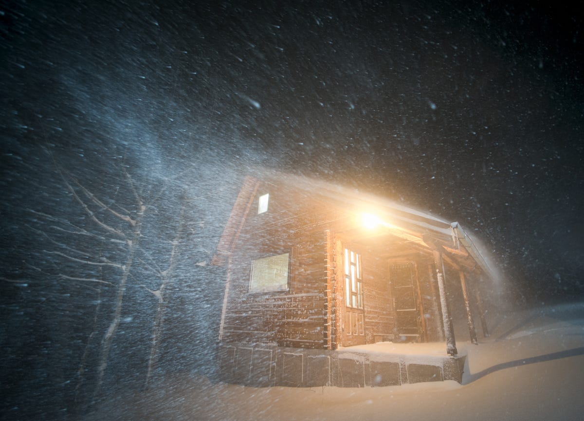 A house with its porch light on in a blizzard.
