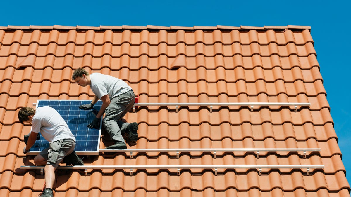 Two people installing a solar panel on a terra cotta style roof.