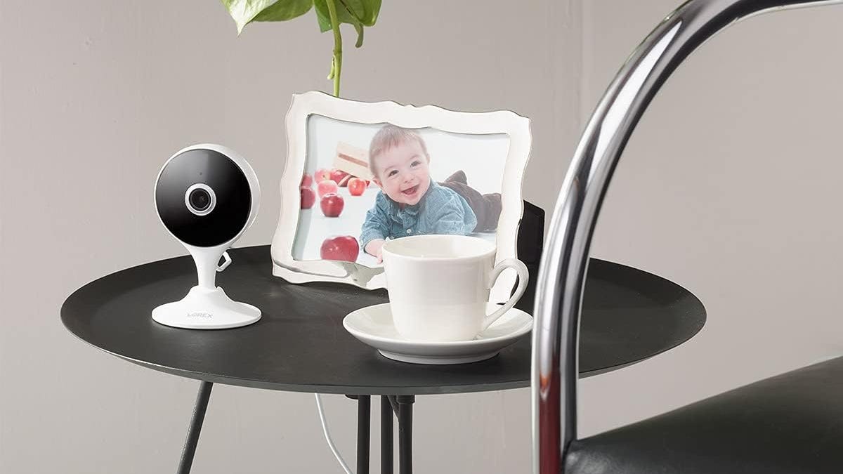 The Lorex indoor security camera sitting on a small black table with a cup and saucer and a child&apos;s photo.