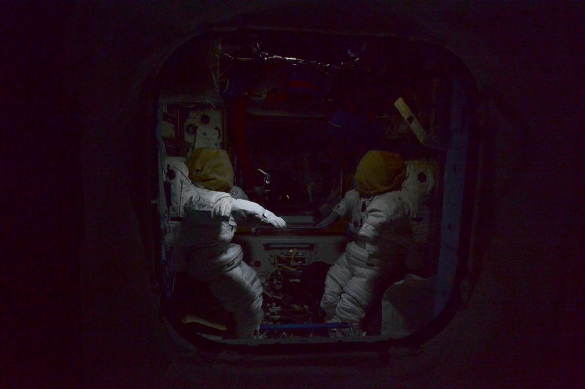 Two empty spacesuits face each other in the dark on the ISS.