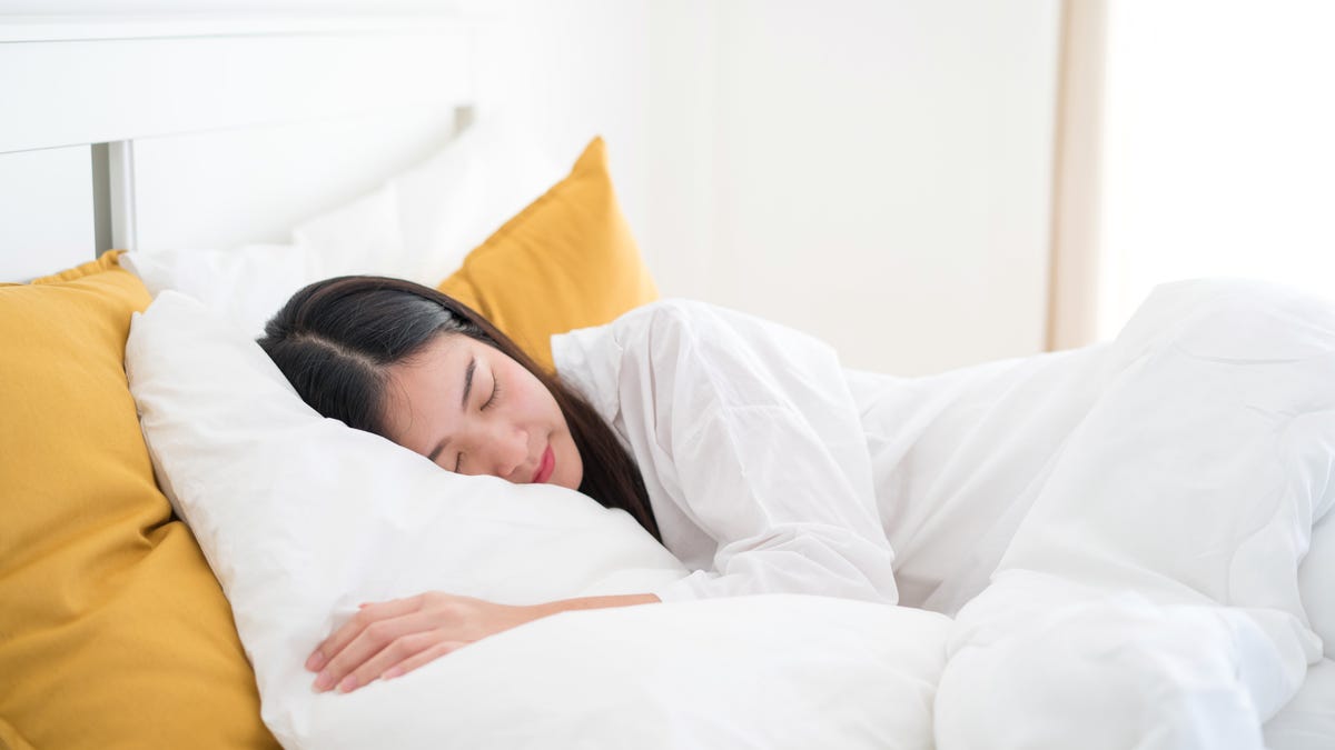 A woman cuddled up and sleeping comfortably with a pile of fluffy pillows