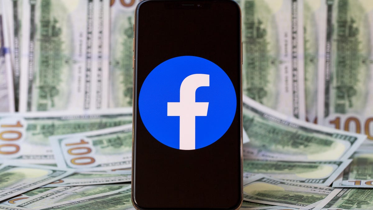 Facebook logo on a smartphone screen against a backdrop of $100 bills.
