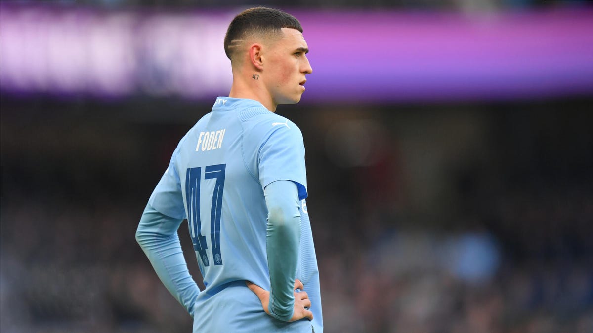 Side on image of Manchester City forward Phil Foden looking straight on with his hands on both hips.