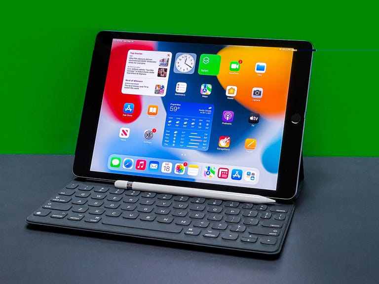 9th Gen iPad with accessories sits on gray surface with green background.