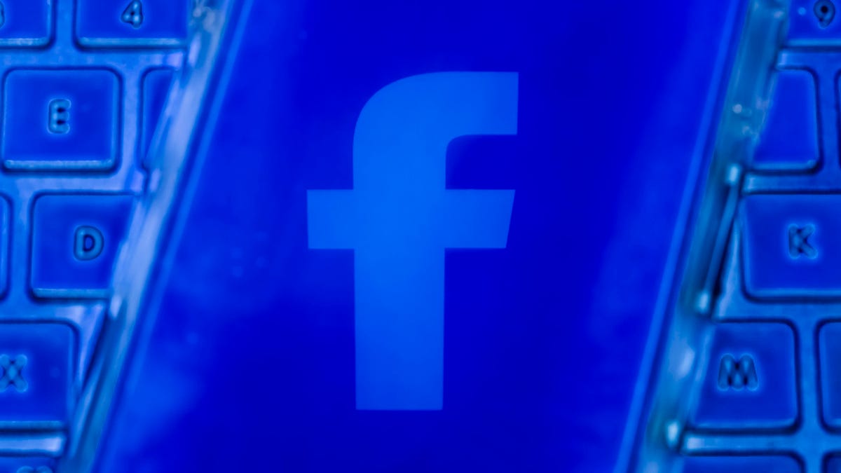 Photo of the Facebook logo on a smartphone screen, on top of a keyboard, all rendered in shades of blue.