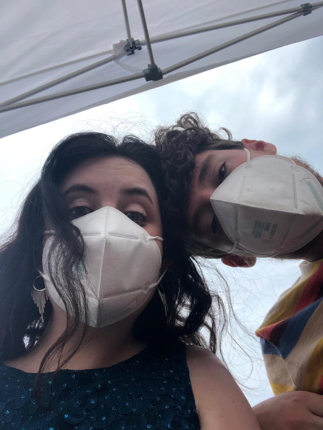A selfie of the author and her partner, both wearing masks. The author wears a dress, and her partner wears a T-shirt.