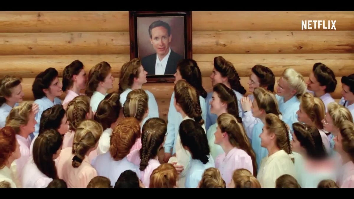 A framed photograph of Warren Jeffs with a group of his wives looking at it.