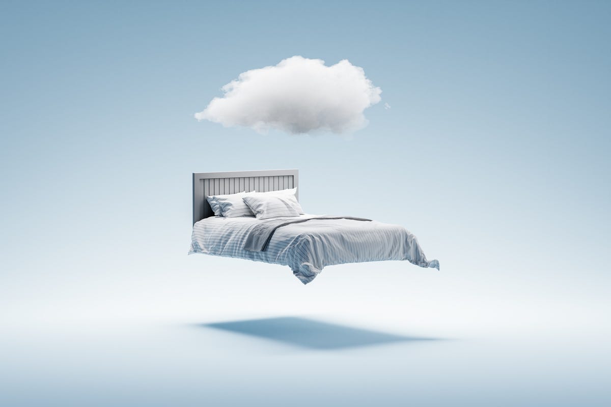Empty bed floats in space with a cloud above it.