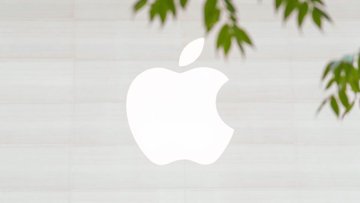 Apple logo on store facade with tree branches protruding into the frame.