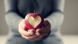 Hands holding an apple with a heart-shaped cutout.