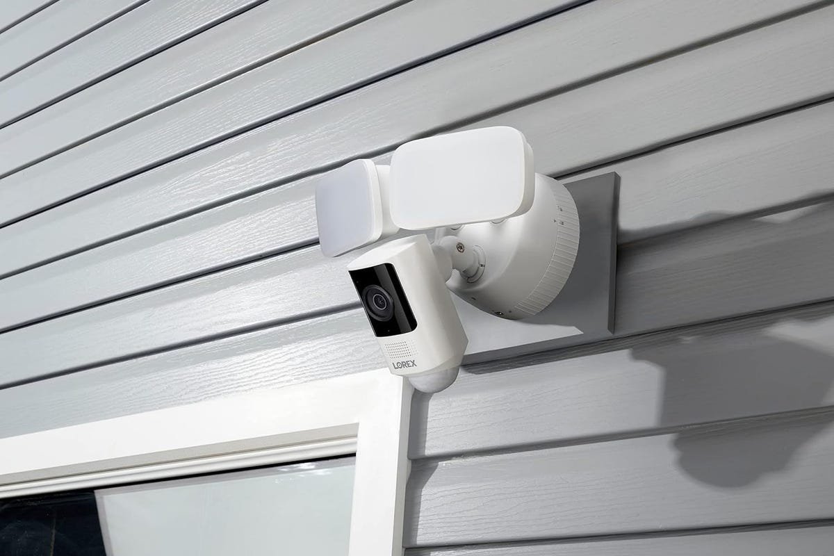 The Lorex floodlight cam mounted on house siding above a glass door.