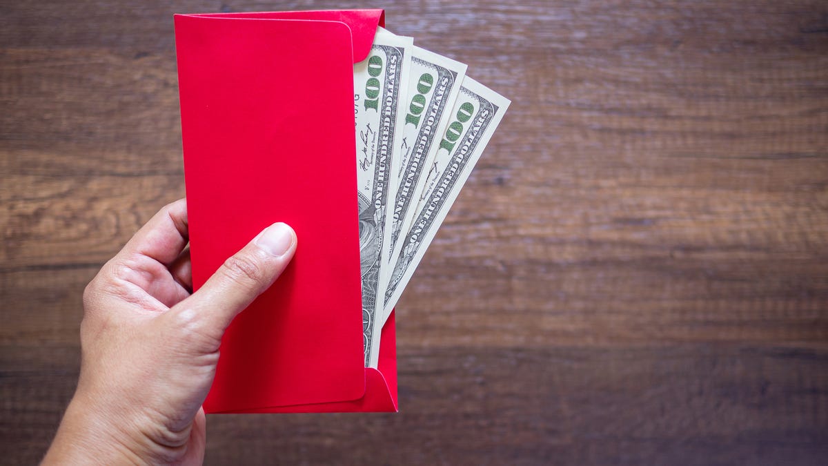 A hand holding a red envelope stuffed with one hundred dollar bills