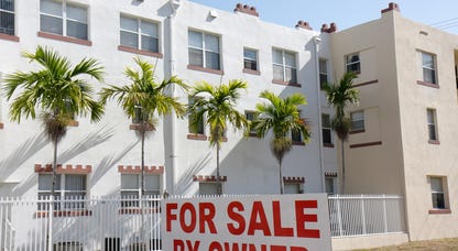 White and tan apartment block with palm trees and sign that says For Sale by Owner