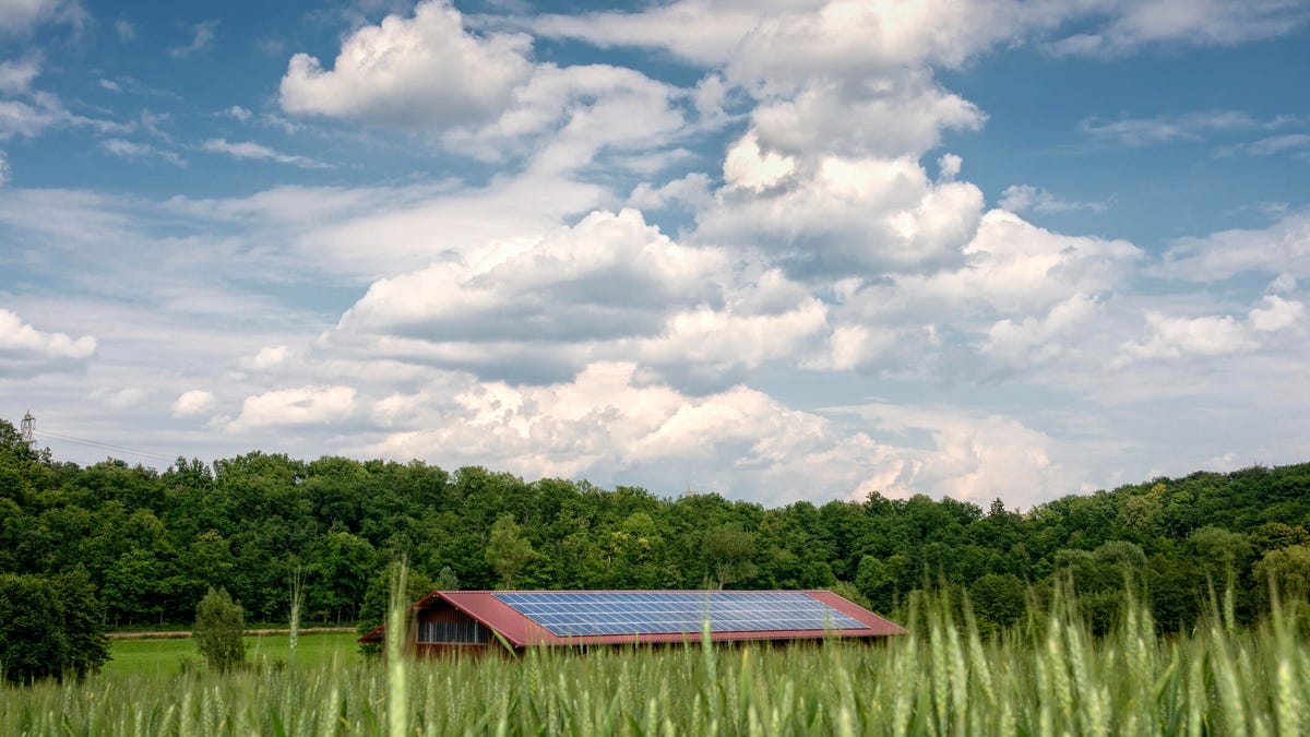 Solar panels on a building in a field under a partly cloudy sky.