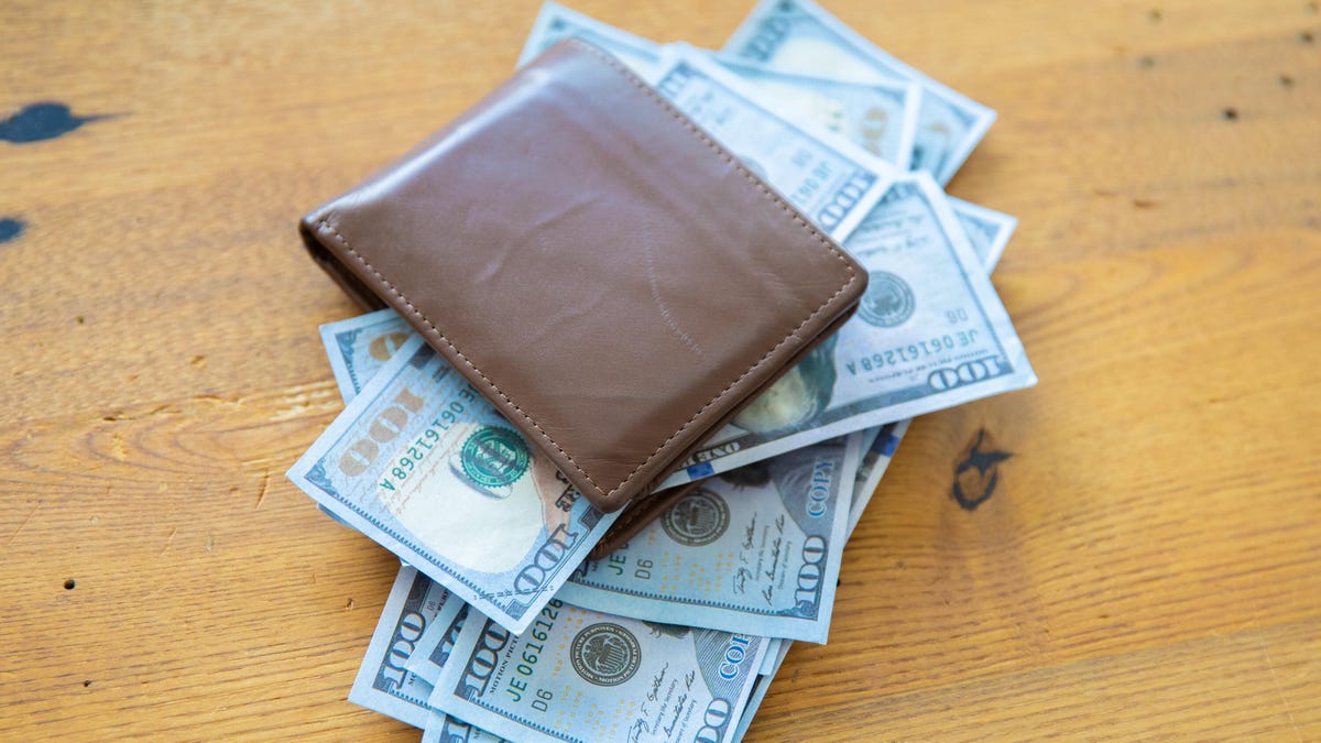 $100 bills bursting out of a brown leather wallet