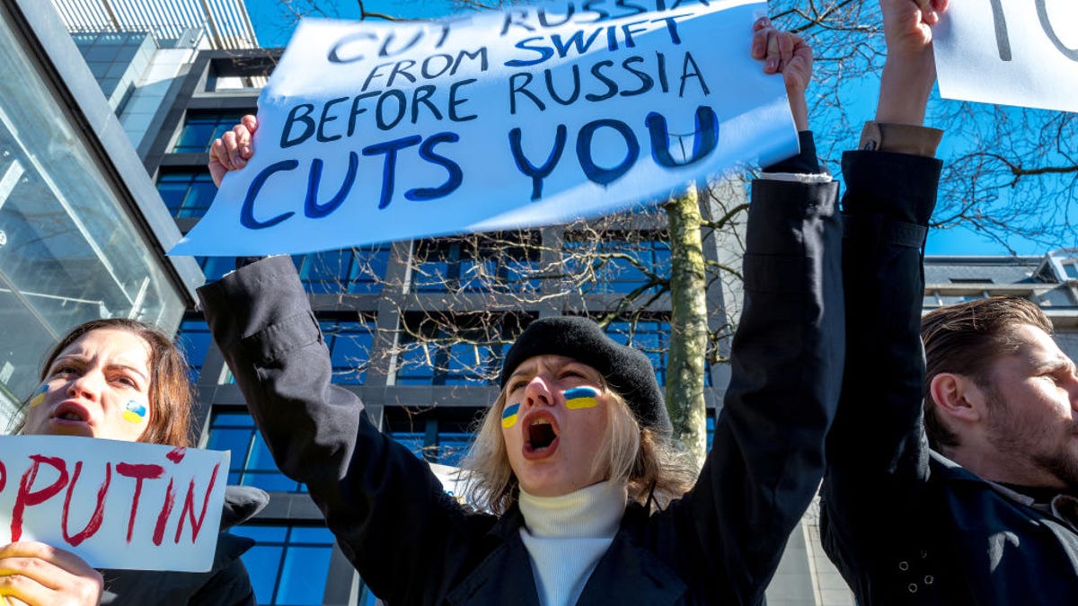 A protester holds a banner calling for Russia to be banned from the SWIFT banking system during a demonstration Saturday against Russia's invasion of Ukraine, held in front the building of the Permanent Mission of Russia to the EU in Brussels.