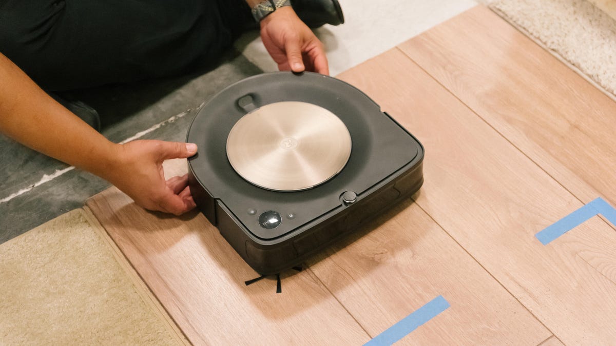 A robot vacuum being placed on a hardwood mat for testing.