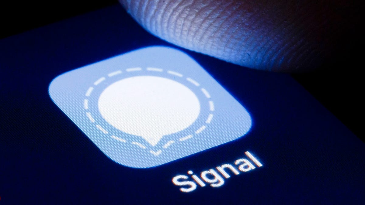 A finger hovers over a phone screen where the icon for the Signal encrypted messenger app is displayed.