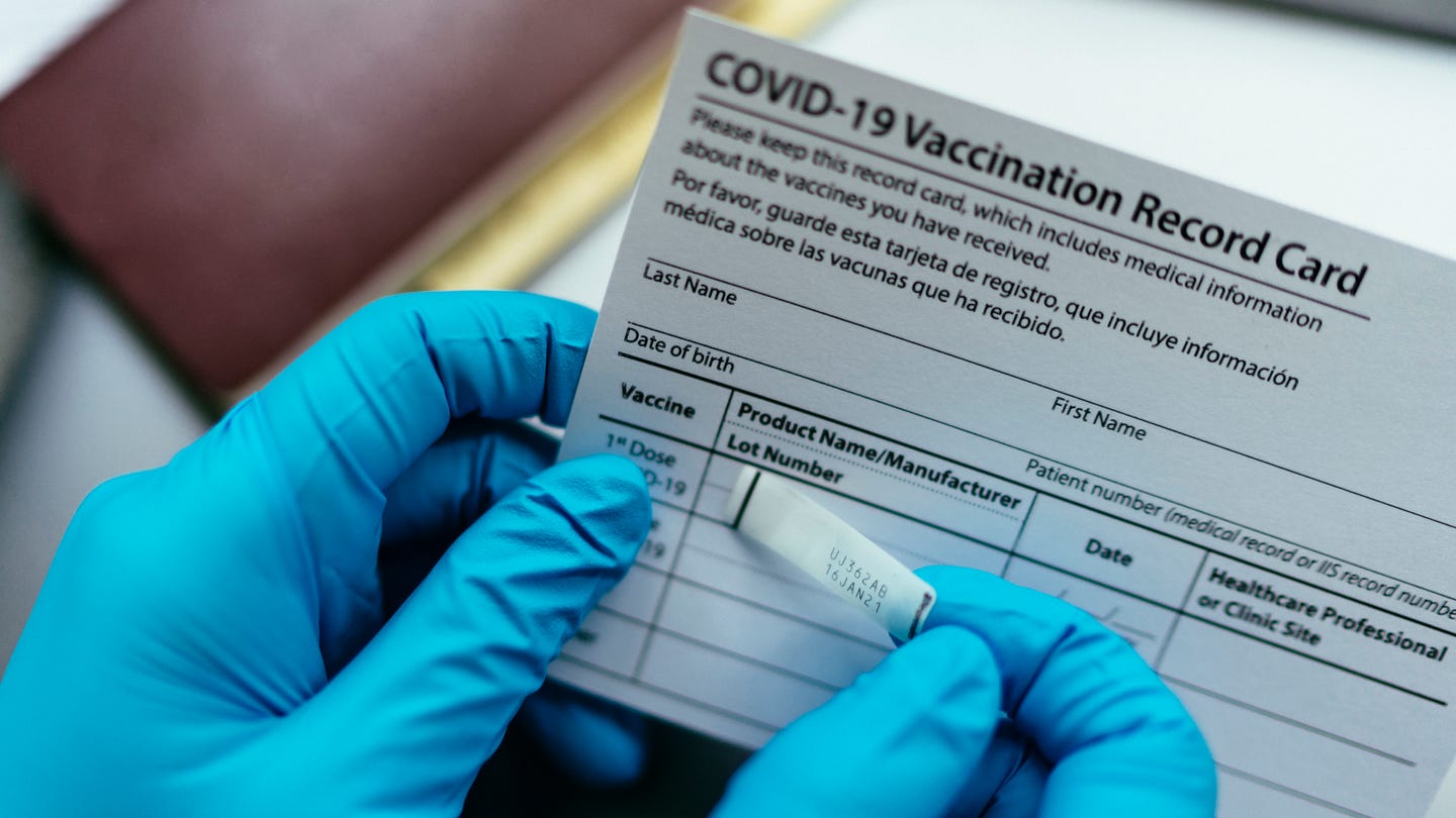 A pair of gloved hands holds a COVID-19 vaccination record card