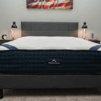 The DreamCloud Hybrid mattress on a gray bed frame with two nightstands next to it.