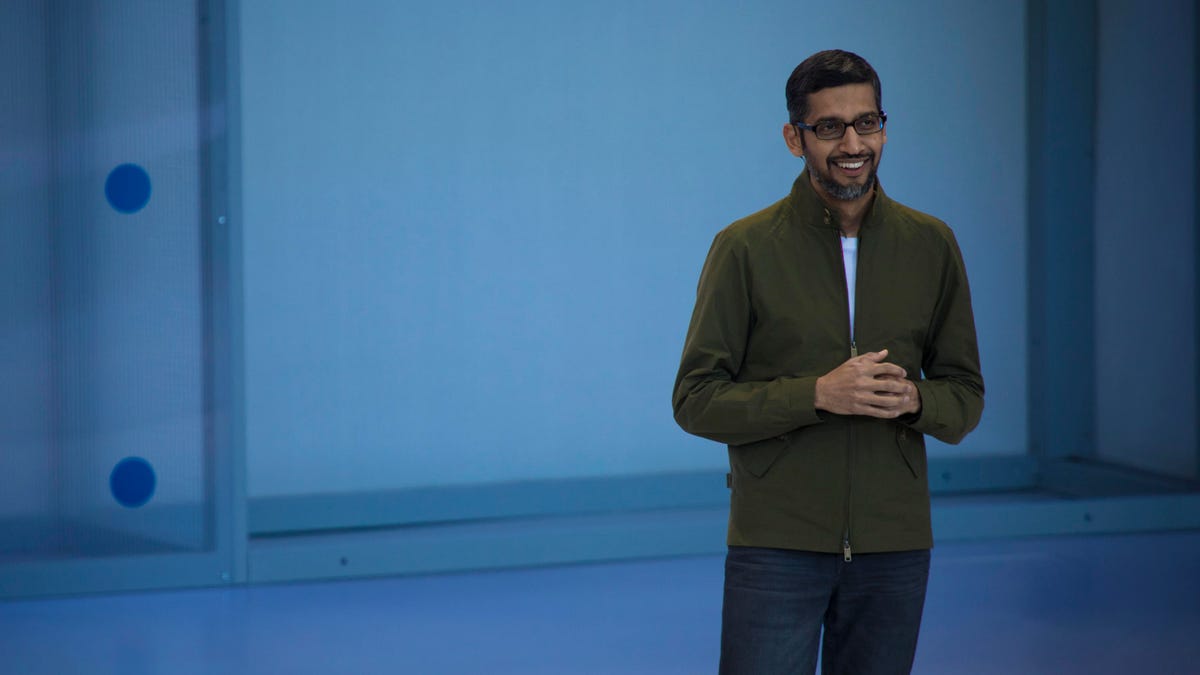 Sundar Pichai in an olive green jacket and jeans, standing onstage at the Shoreline Amphitheater Mountain View.