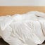 A Brooklinen down comforter covering a mattress on a wooden bed frame.