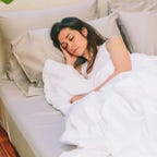 A woman cuddled up to a Nest Bedding Silk comforter while laying in bed.