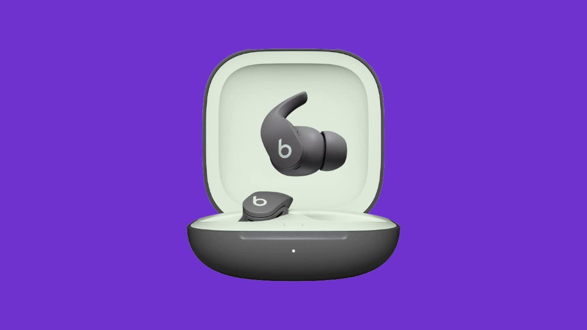 A pair of grey Beats Fit Pro earbuds and charging case against a purple backgound.