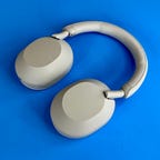 A pair of white Sony WH-1000XM5 headphones against a blue background