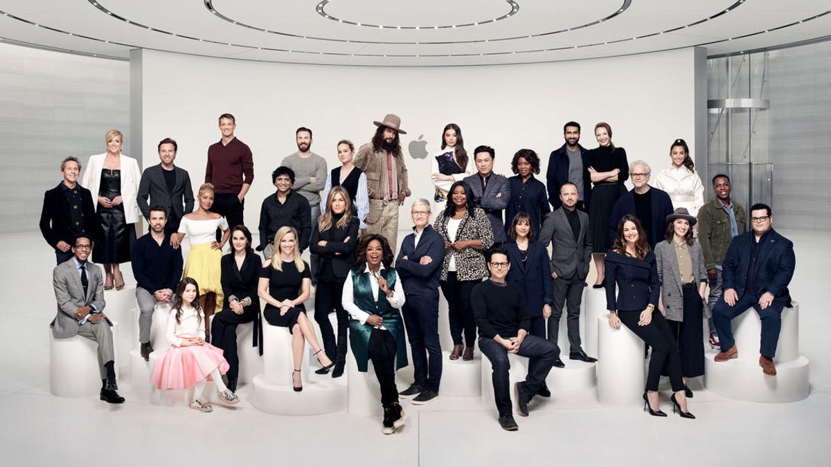 A group of more than 30 stars stand in a clean white Apple lobby
