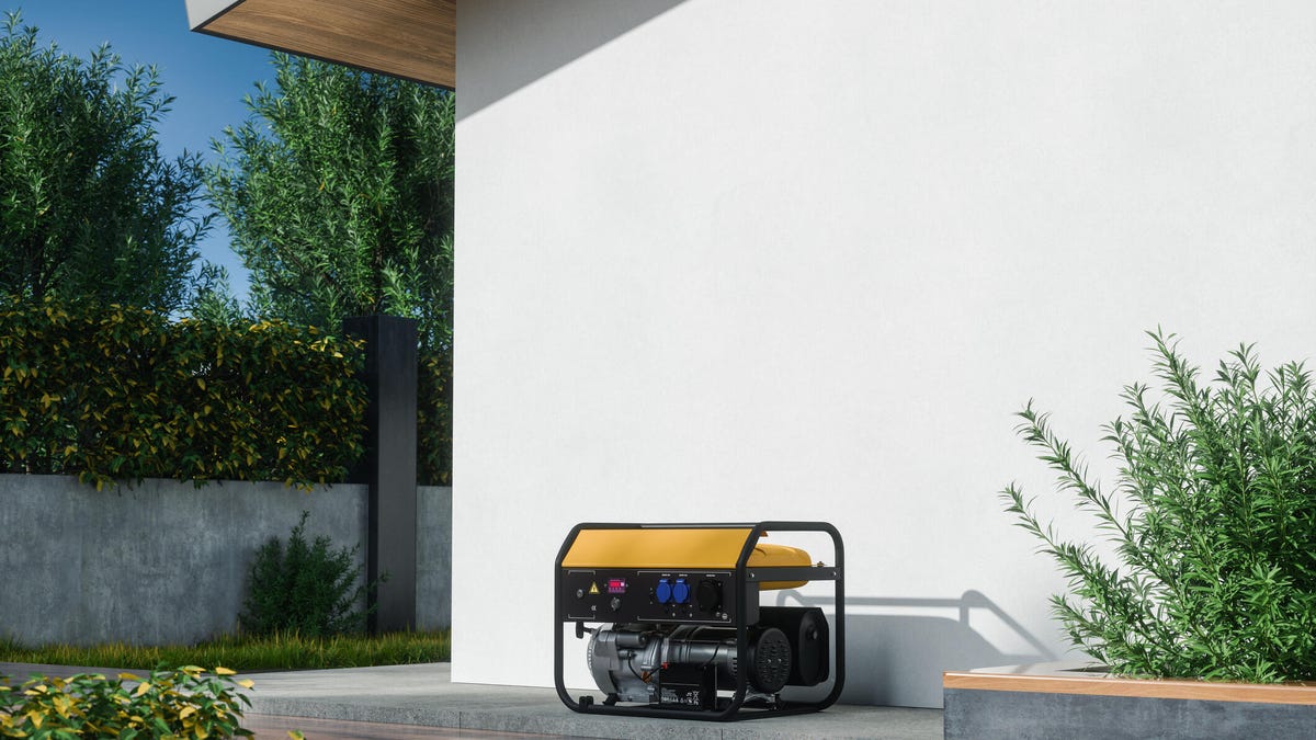 A yellow and black generator sitting on the ground against a white, exterior home wall.