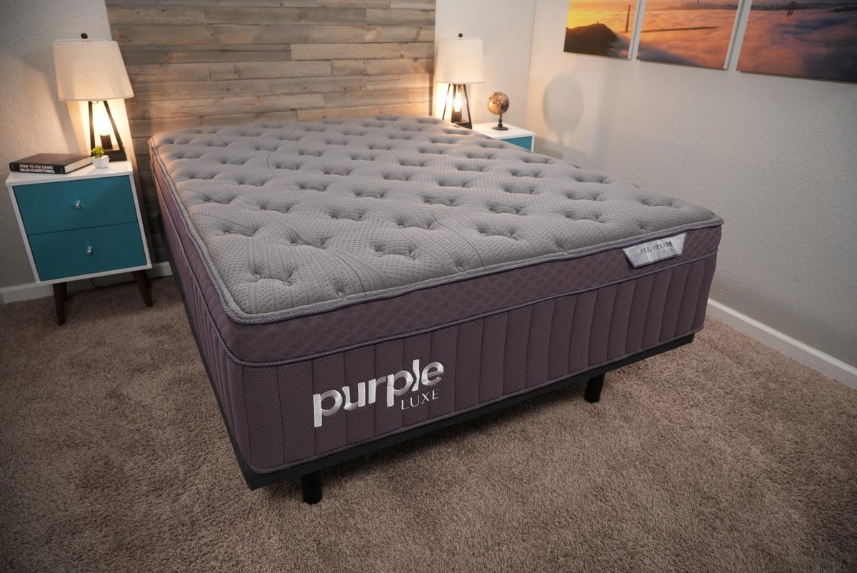 The Purple mattress on a black bed frame in a warmly lit room.